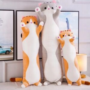 Drei große Katzenstofftier-Kissen stehen vor gerahmten Bildern an einer Wand.