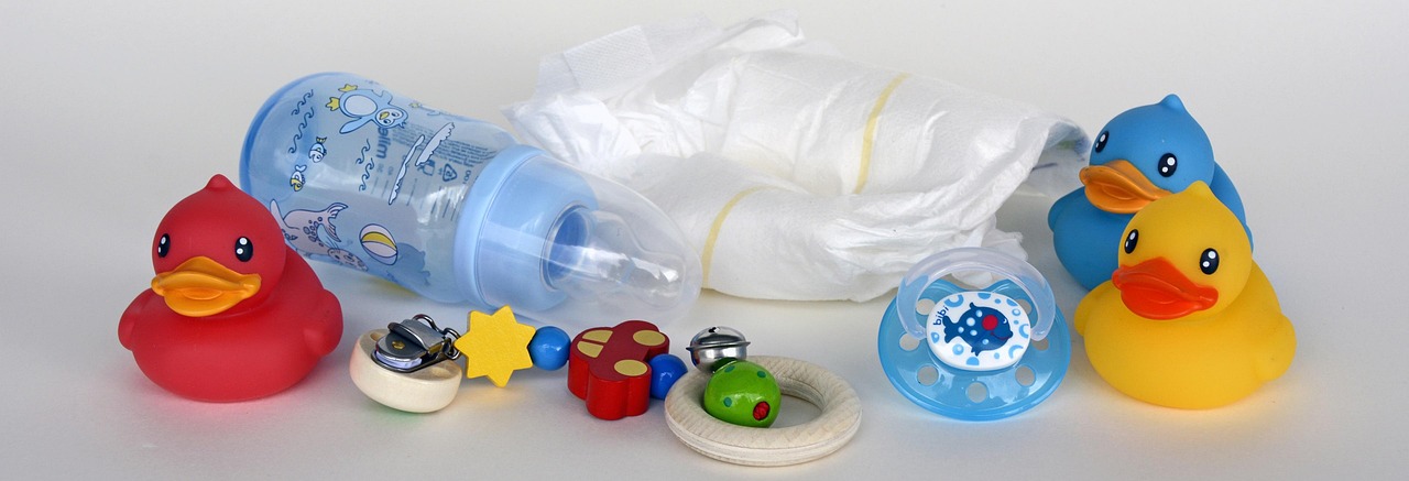 Verschiedene bunte Babyartikel, darunter Gummienten, Schnuller, Windel und eine Babyflasche.