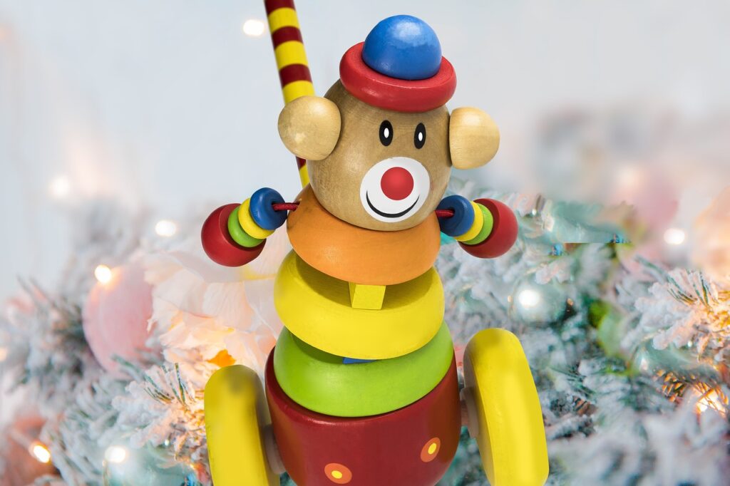 Buntes Holzspielzeug in Clownform vor festlich dekoriertem Weihnachtsbaum.
