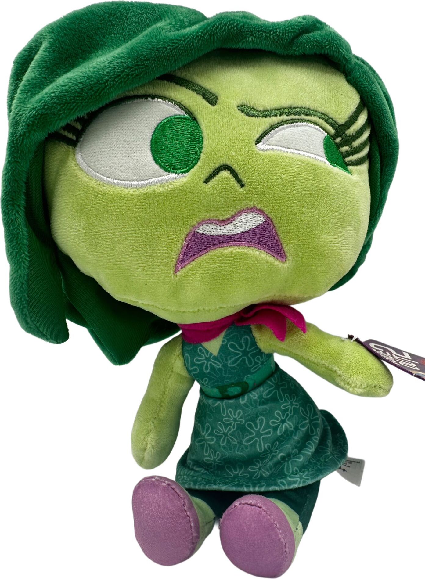 Grüne Plüschfigur mit ausdrucksstarkem Gesicht und lila Schuhen.