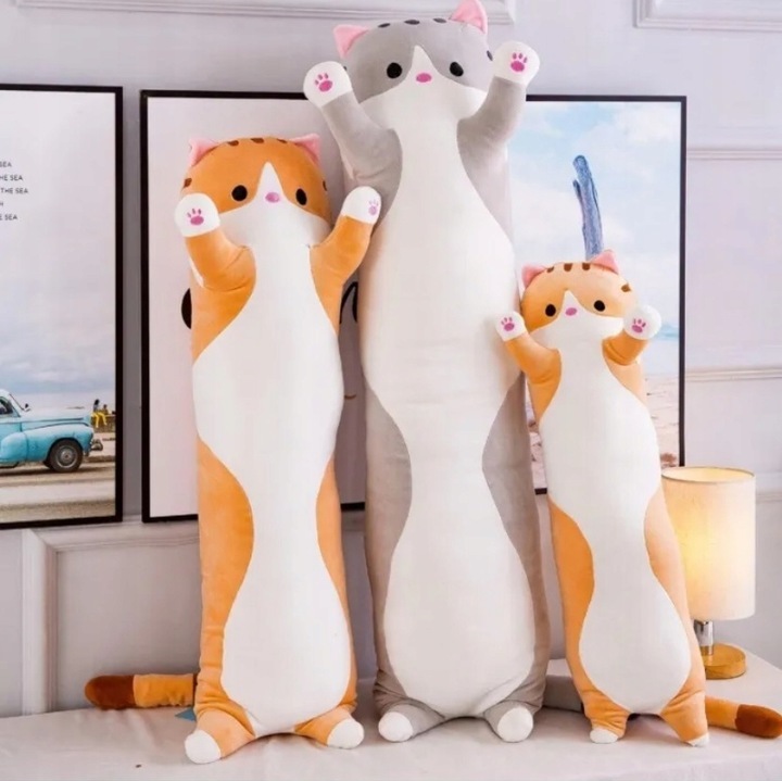 Drei große Katzenstofftier-Kissen stehen vor gerahmten Bildern an einer Wand. Drei große Katzenstofftier-Kissen stehen vor gerahmten Bildern an einer Wand.